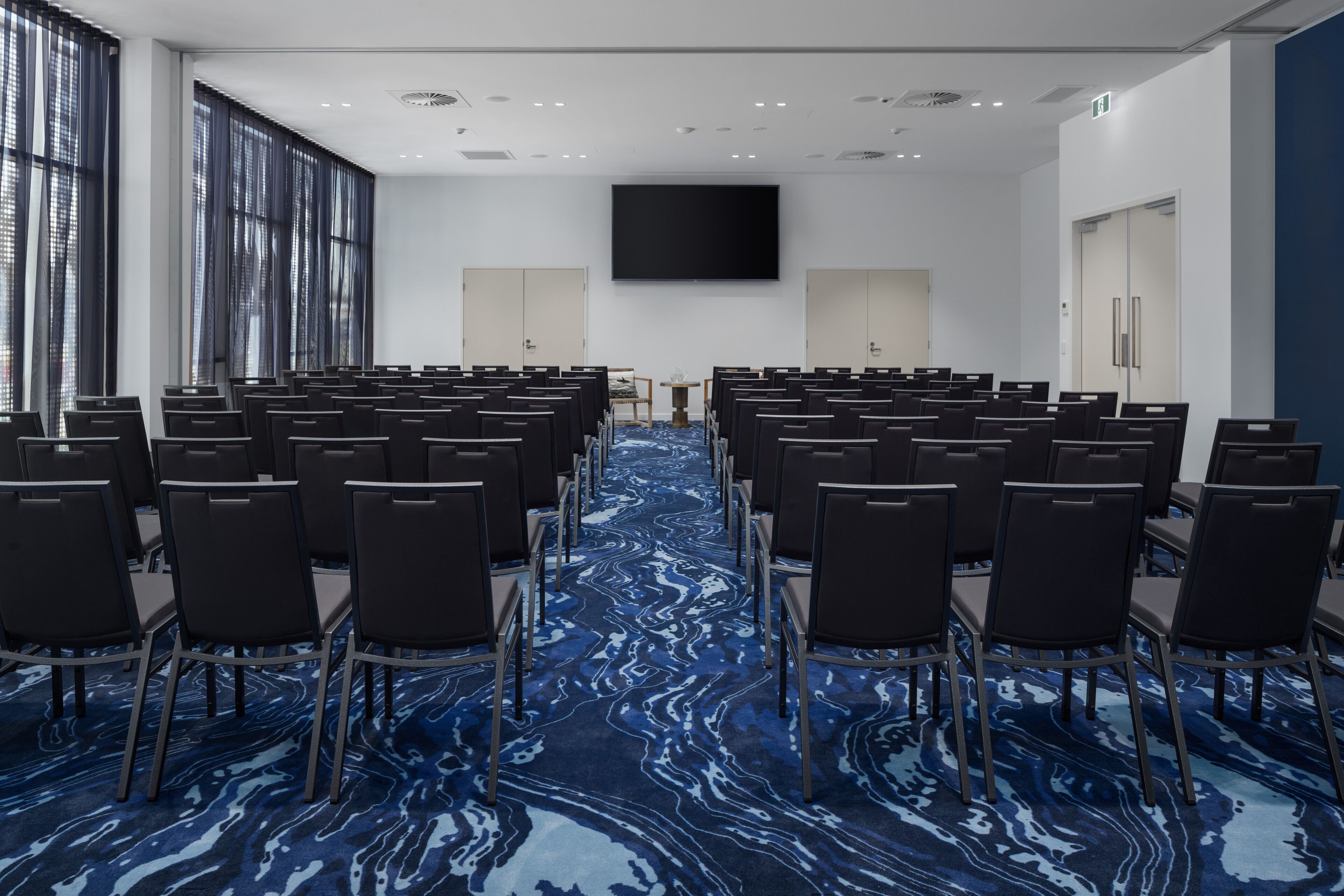 A conference room with rows of chairs, a large screen, and a blue patterned carpet.
