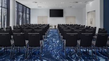 A conference room with rows of chairs, a large screen, and a blue patterned carpet.