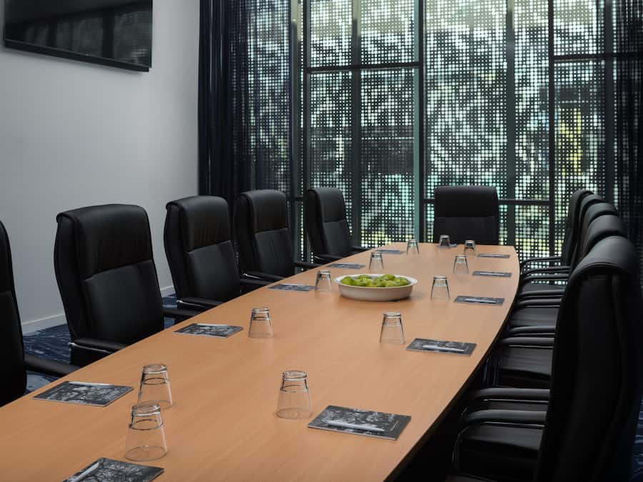 A conference room with a long table, black chairs, and a large window with a view of buildings.
