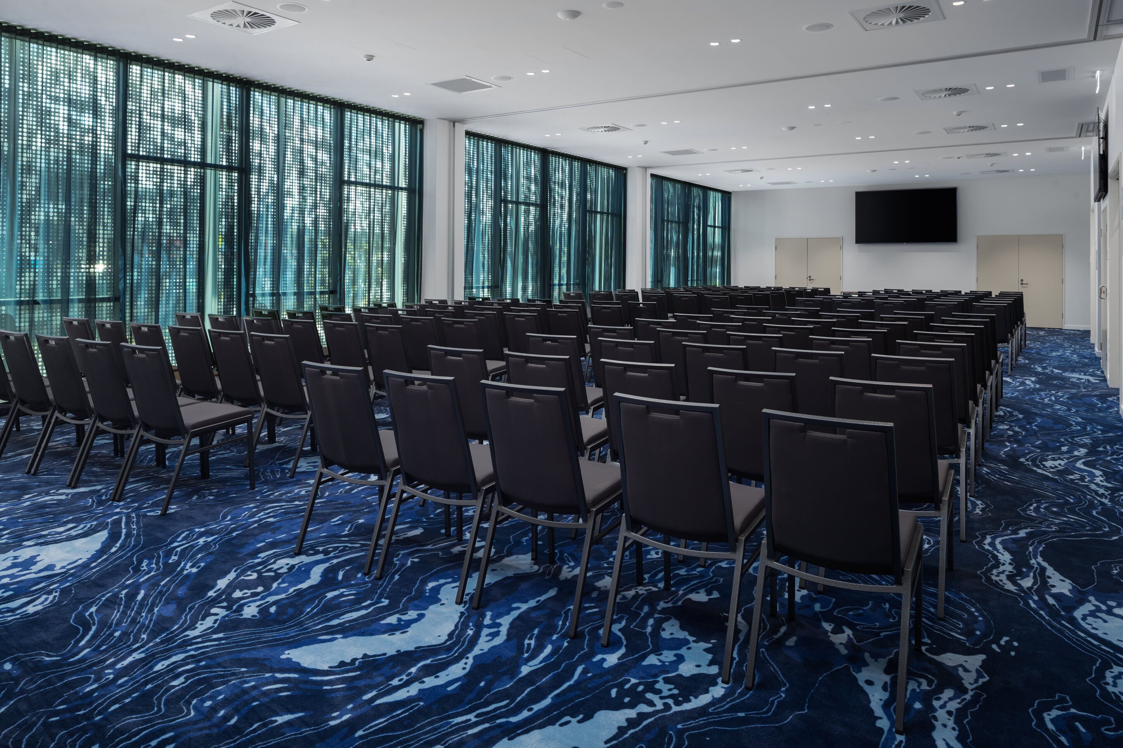 A conference room with rows of chairs, large windows, and a flat-screen TV.