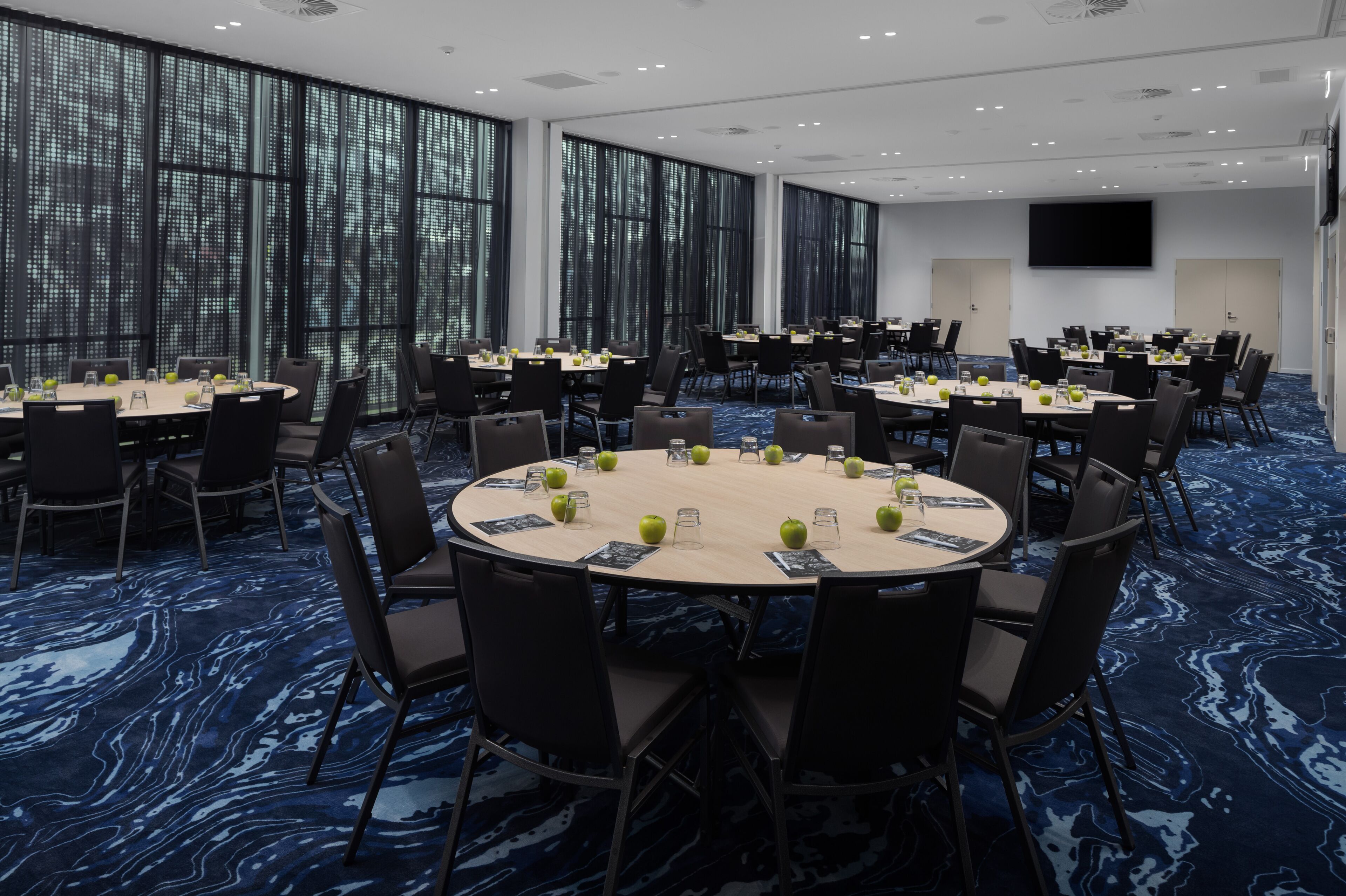 A conference room with round tables, black chairs, and a large screen.