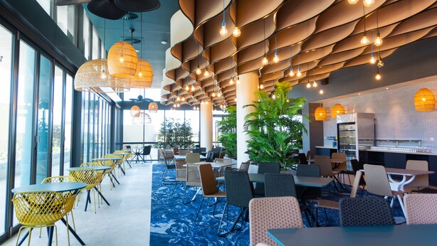 A modern restaurant with a blue carpet, yellow chairs, and a ceiling with hanging lights.