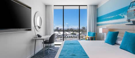 Une chambre d’hôtel dotée d’un grand lit, d’un bureau, d’une chaise, d’une télévision et offrant une vue sur la ville grâce à de grandes fenêtres.