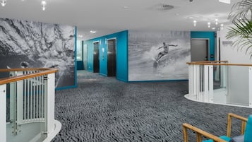 A modern hotel lobby with a wave-patterned carpet, a large cityscape mural, and a wooden railing.