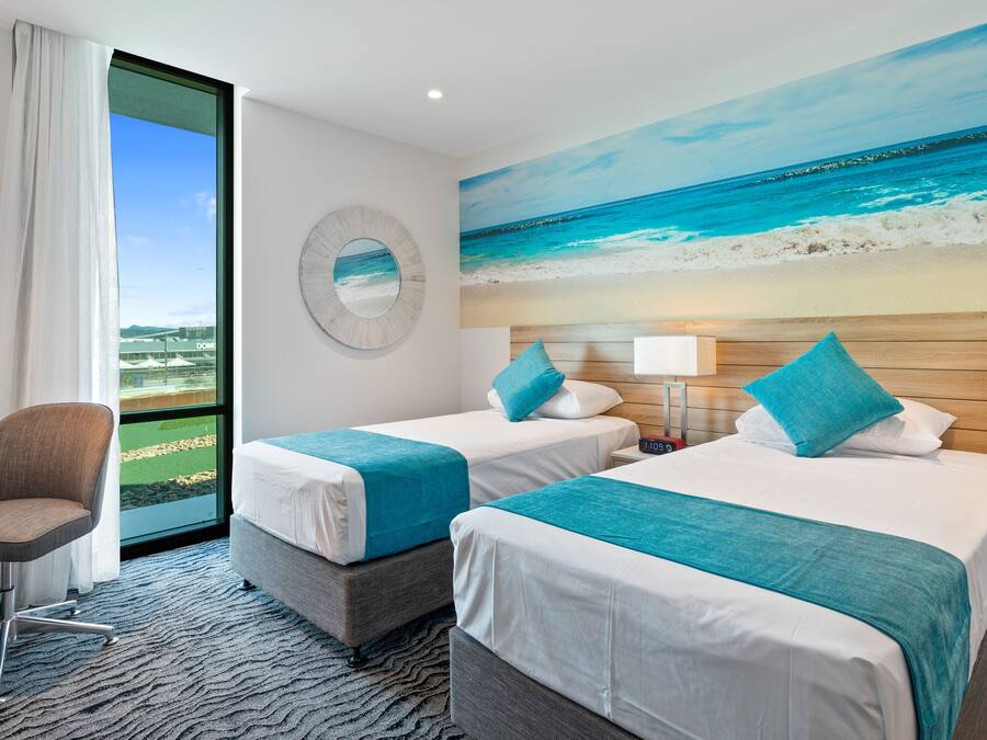 A hotel room with two beds, a desk, and a large window with a view of the beach.