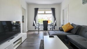 Una sala de estar moderna con un televisor de pantalla plana, un sofá gris, una mesa de centro y una zona de comedor con una mesa y sillas.