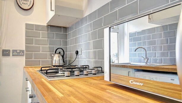 Una cocina moderna con salpicadero de azulejos grises, encimera de madera, cocina a gas y horno empotrado.