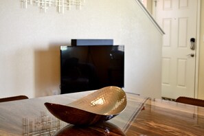 Taula de menjador amb un centre de decoració en un bol, televisió al fons i una escala que condueix a un nivell superior.