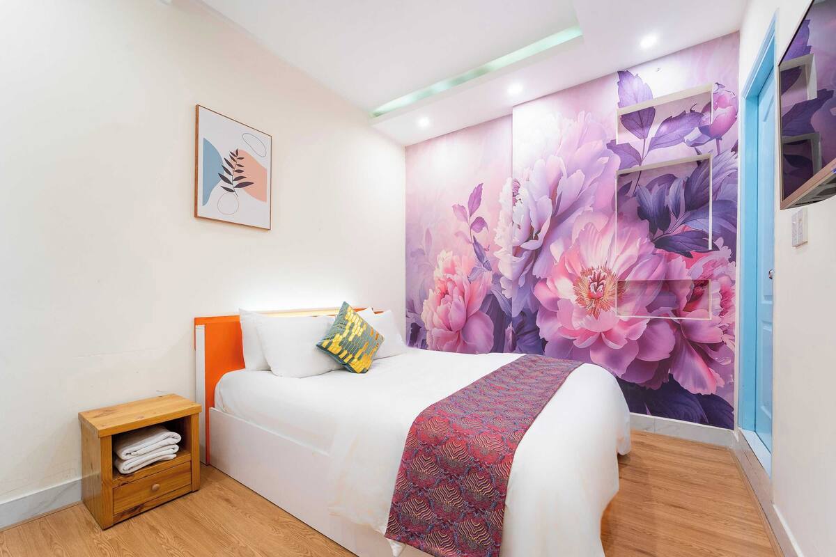 A bedroom with a bed, a nightstand, a wall-mounted shelf, and a floral wallpaper.
