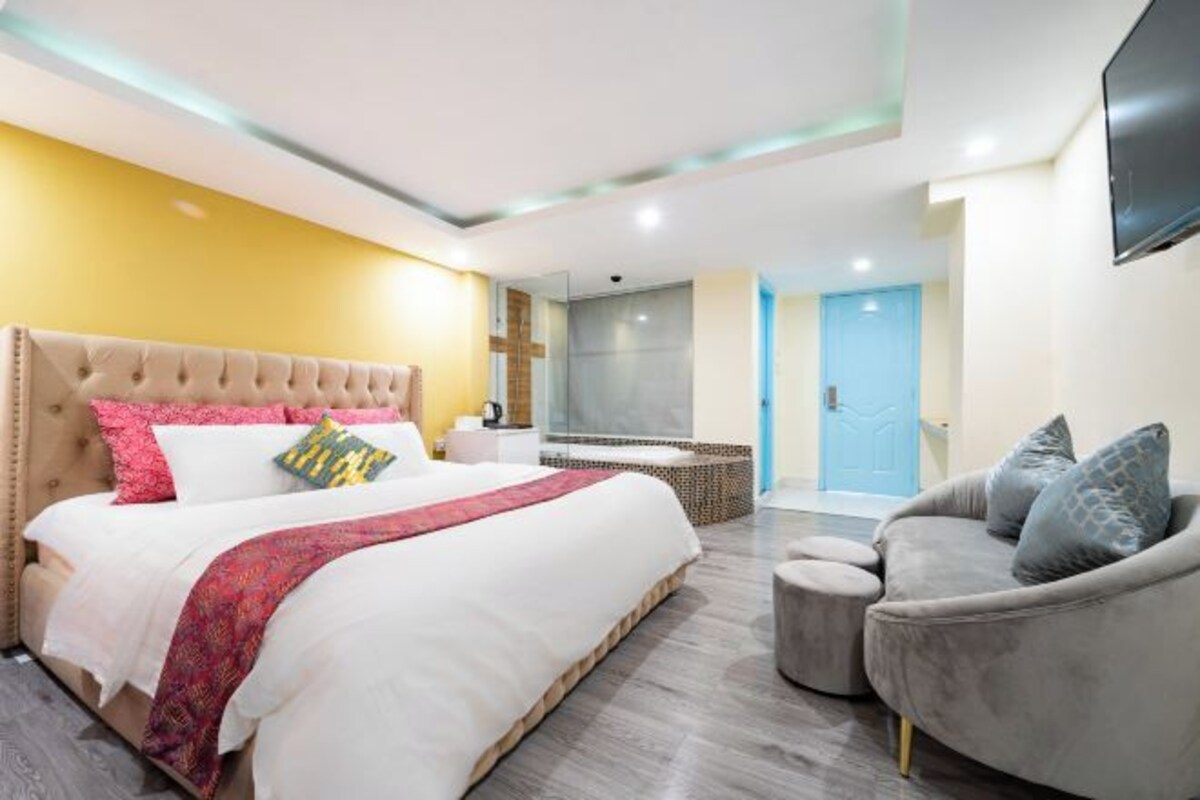 A modern bedroom with a large bed, a grey sofa, and a TV mounted on the wall.