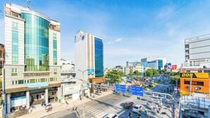 A modern building with a curved glass facade, a prominent sign for 'LONG MA BUILDING', and a busy street with vehicles and pedestrians. - Collection O Joy Inn - Near T3 Terminal (Ho Chi Minh City)