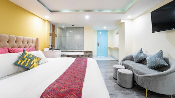 A modern hotel room with a large bed, a grey sofa, a TV mounted on the wall, and a bathroom visible through an open door. - Collection O Joy Inn - Near T3 Terminal (Ho Chi Minh City)
