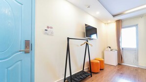 A room with a blue door, a television mounted on the wall, a small white cabinet, and two orange stools. - Collection O Joy Inn - Near T3 Terminal (Ho Chi Minh City)