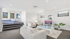 Ein modernes Wohnzimmer mit einer Couch, einem Couchtisch, einem Fernseher und einer Treppe, die auf einen Balkon führt.