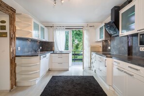 A modern kitchen with white cabinetry, a black countertop, and a view of greenery outside.