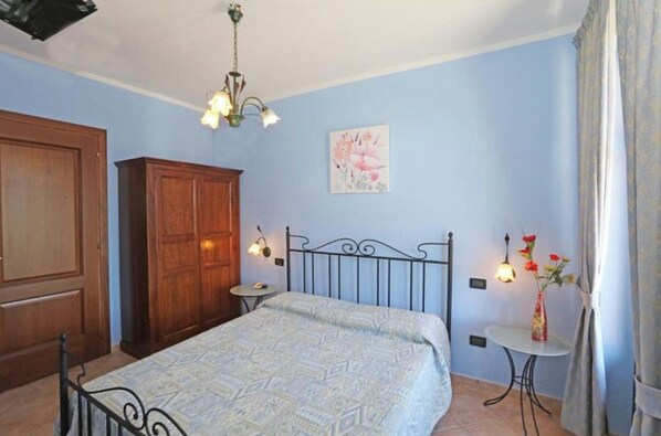 Ein Schlafzimmer mit Bett, Kleiderschrank, kleinem Tisch mit Lampe und Wandleuchte.