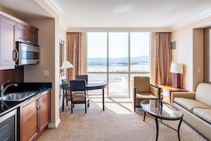 A hotel room with a kitchen, dining area, and a balcony with a view of the beach.