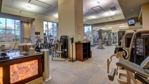 Et fitnesscenter med forskellige træningsmaskiner, en receptionsdisk og store vinduer, der lukker naturligt lys ind.