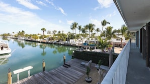 A marina with boats docked, a wooden deck, and a view of palm trees and buildings.