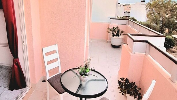A balcony with a table and chairs, potted plants, and a view of the cityscape. - Domus Dulcis Domus (Limenas Chersonisou)