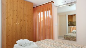 Un dormitorio con un armario de madera, una cama con colcha estampada y un baño visible a través de un espejo.