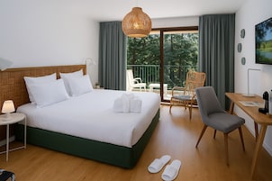 Habitación de hotel con cama, escritorio, silla y balcón con vista a árboles.