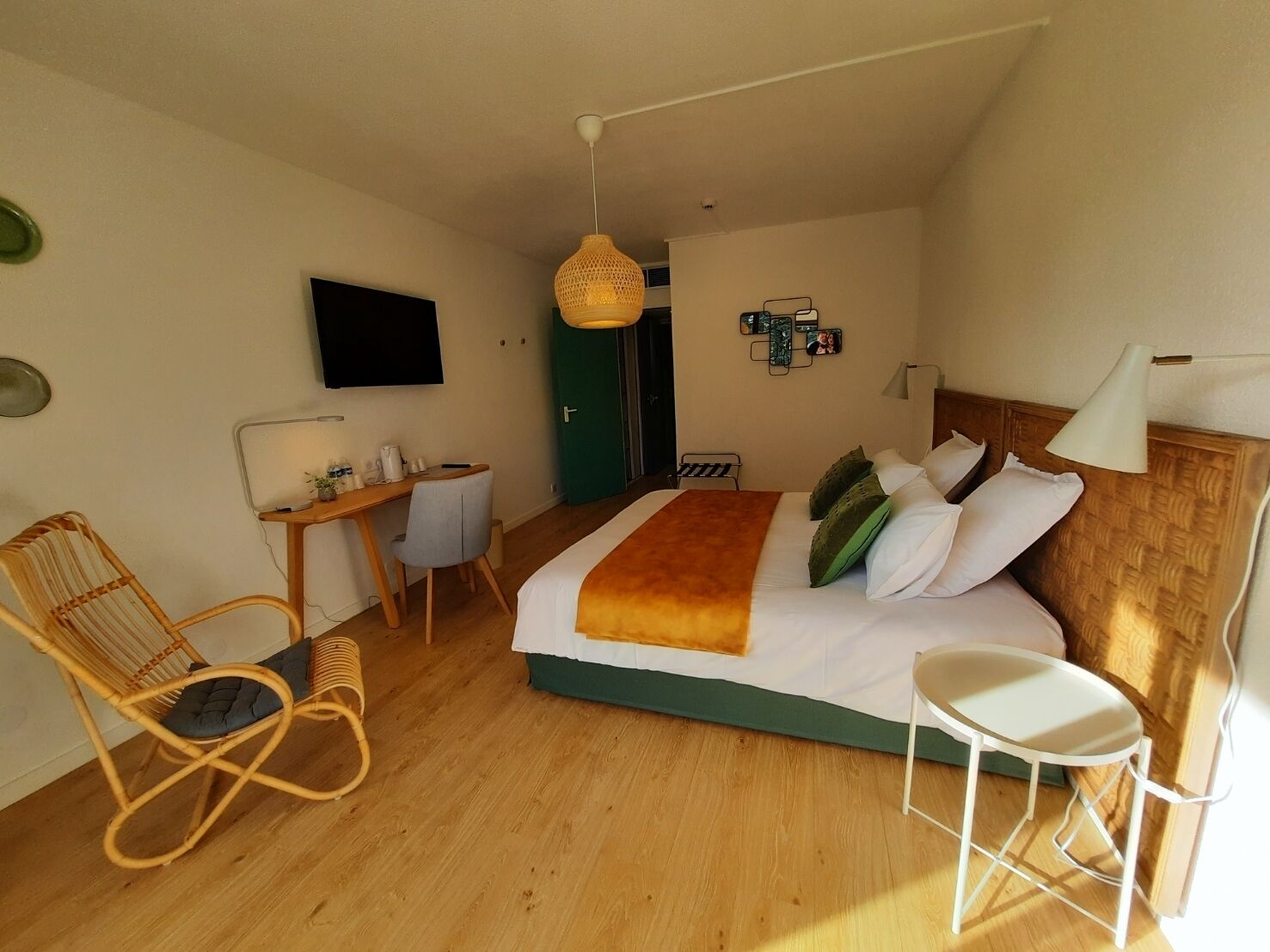 A bedroom with a bed, a desk, a chair, a TV, and a hanging light fixture.