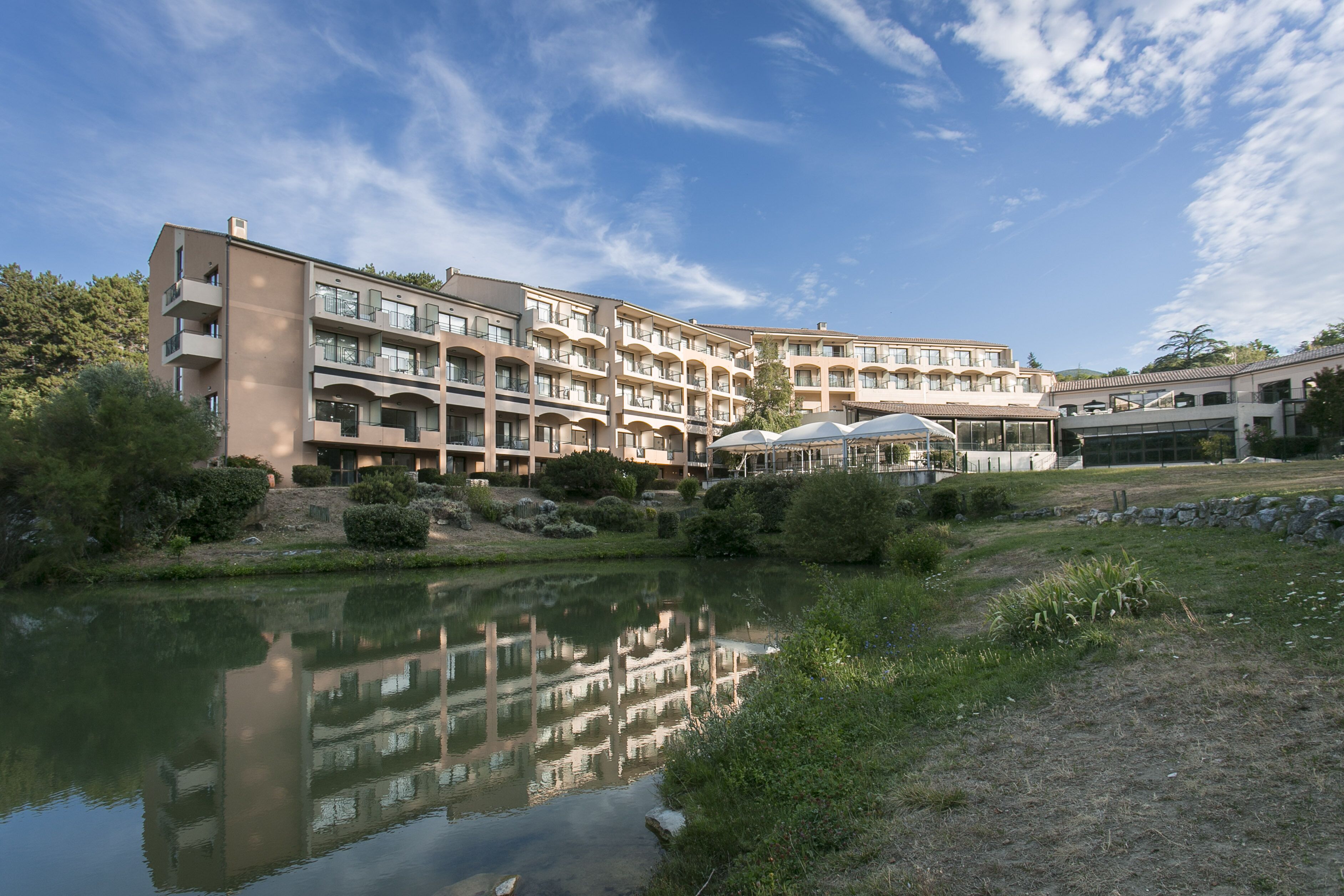 A multi-story hotel with balconies, a reflection pool, and a landscaped garden.