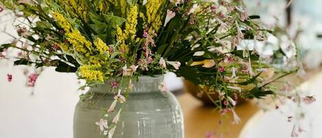 Vista despejada de una habitación con una mesa de madera, un florero con flores y una lámpara al fondo.