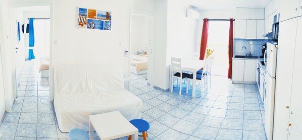 A compact hotel room with a bed, a small table, a chair, a kitchenette, and a bathroom visible through an open door. - Domus Dulcis Domus (Limenas Chersonisou)