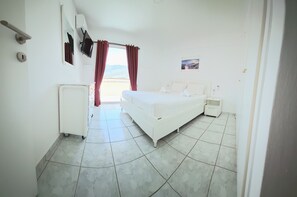 A hotel room with a bed, bedside tables, a small cabinet, a mirror, and a window with curtains. - Domus Dulcis Domus (Limenas Chersonisou)