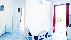 Een lichte kamer met een witte bank, een klein tafeltje en een televisie aan de muur.