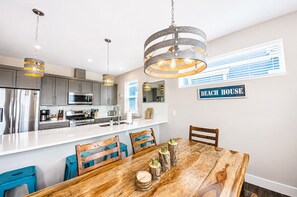 A modern kitchen with stainless steel appliances, a wooden dining table, and a sign indicating a beach house.