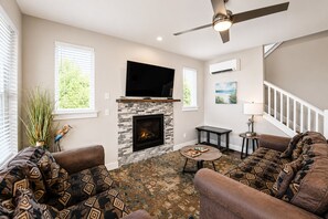 A living room with a fireplace, a flat-screen TV, a ceiling fan, and patterned furniture.
