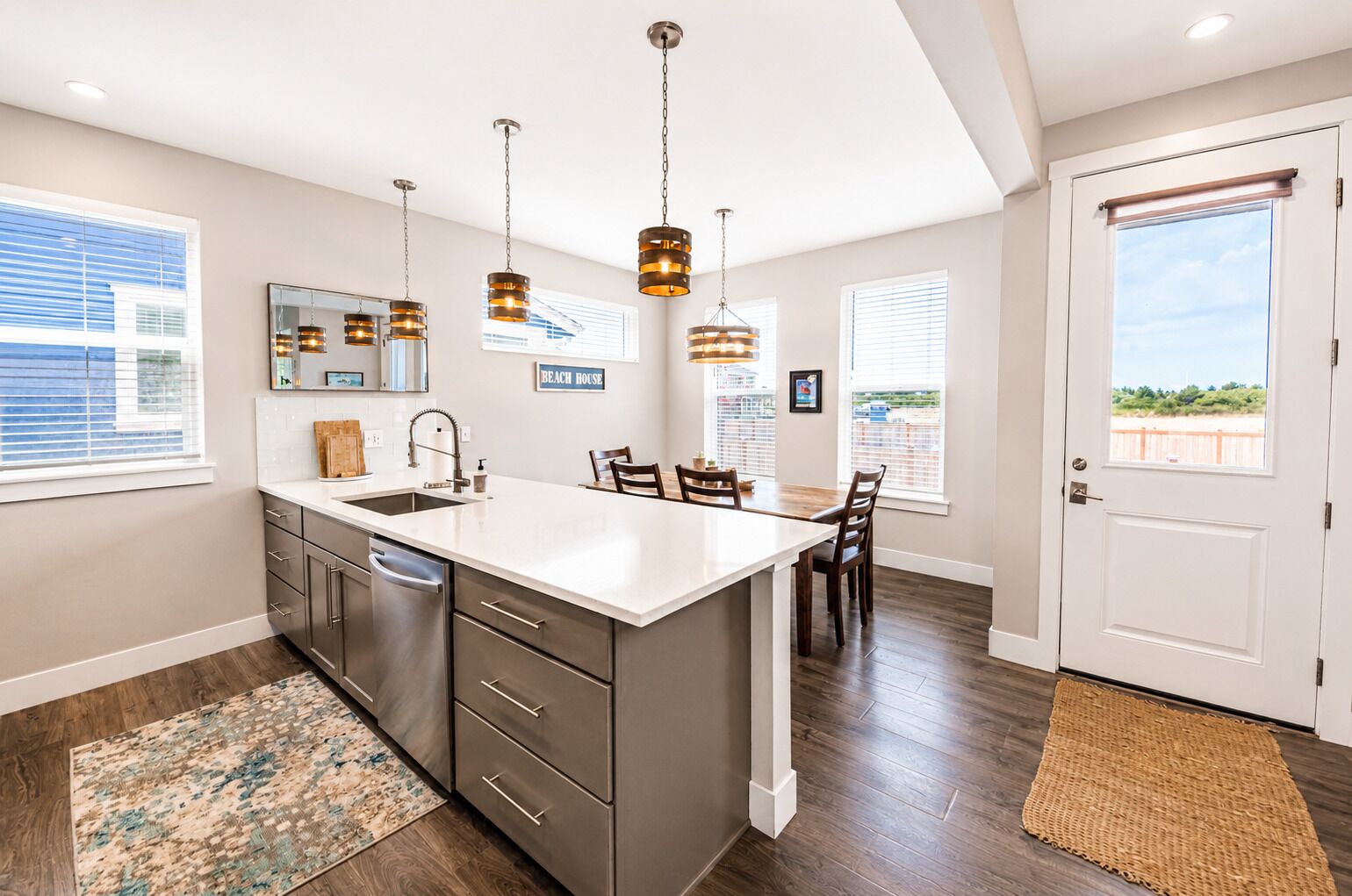 A modern kitchen with a large island, pendant lights, and a view of the beach.