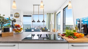 A modern kitchen with a large island, hanging lights, and a view of the sea. - Villa Seemööv - waterfront, terrace, whirlpool, sauna, fireplace, e-charging (Olpenitz)
