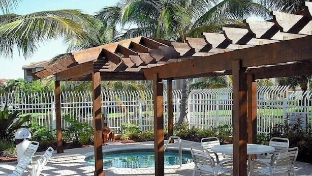 Ein überdachter Außenbereich mit Pool, weißen Stühlen und einer Pergola.