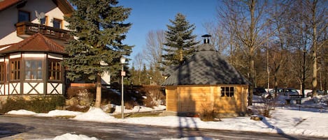 A two-story house with a balcony, a small wooden structure, and snow on the ground.