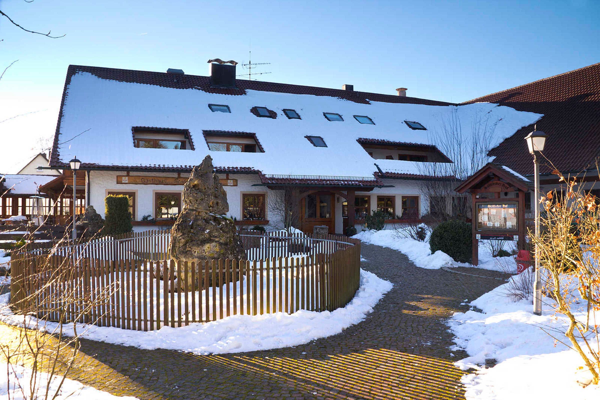 Un bâtiment dont le toit est recouvert de neige, doté d’une entrée pavée et d’une clôture en bois.