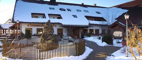 A building with a snow-covered roof, a paved entrance, and a wooden fence.