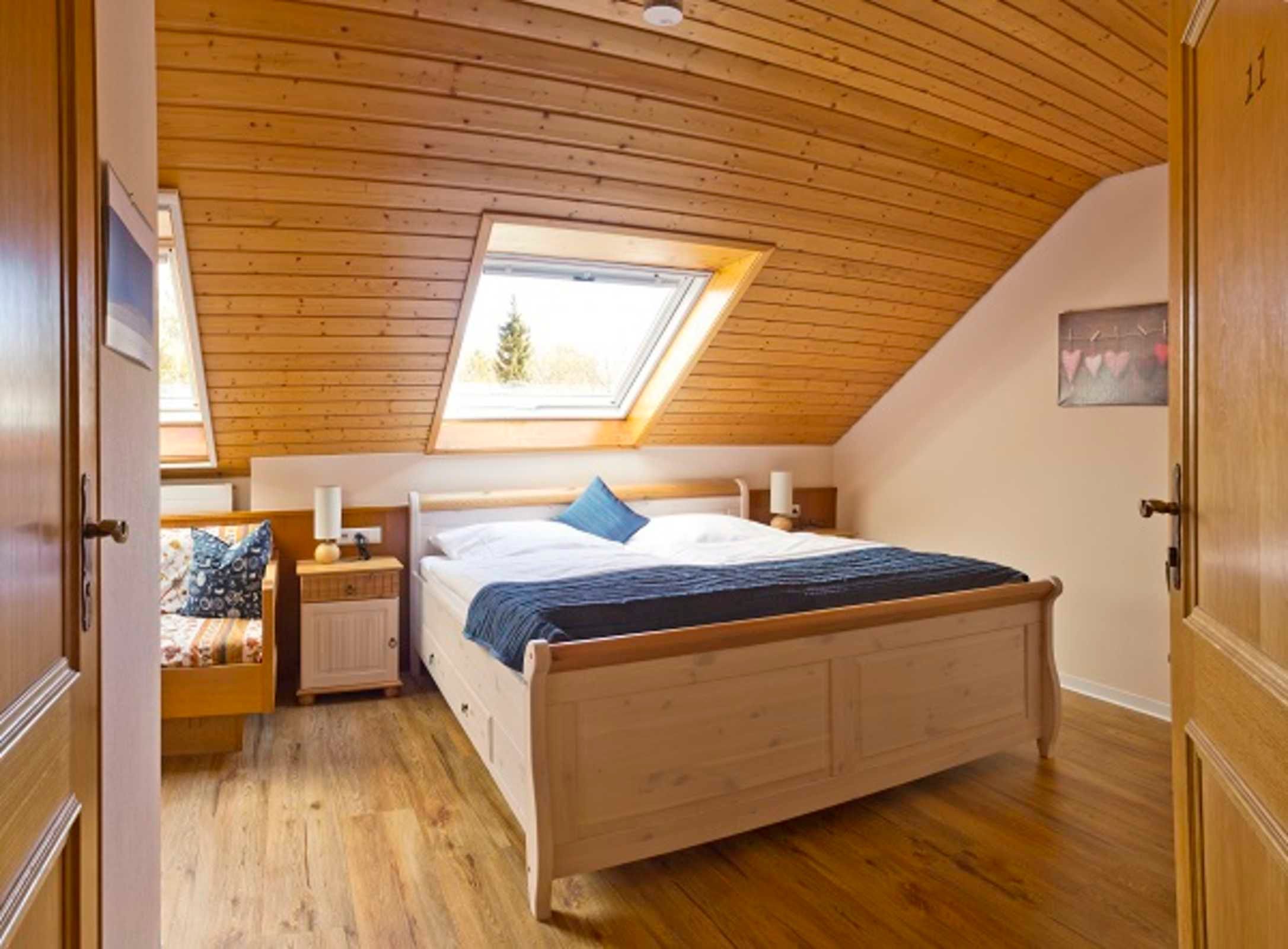 A bedroom with a sloped ceiling, a skylight, a bed with a blue blanket, a nightstand, and a wall-mounted lamp.