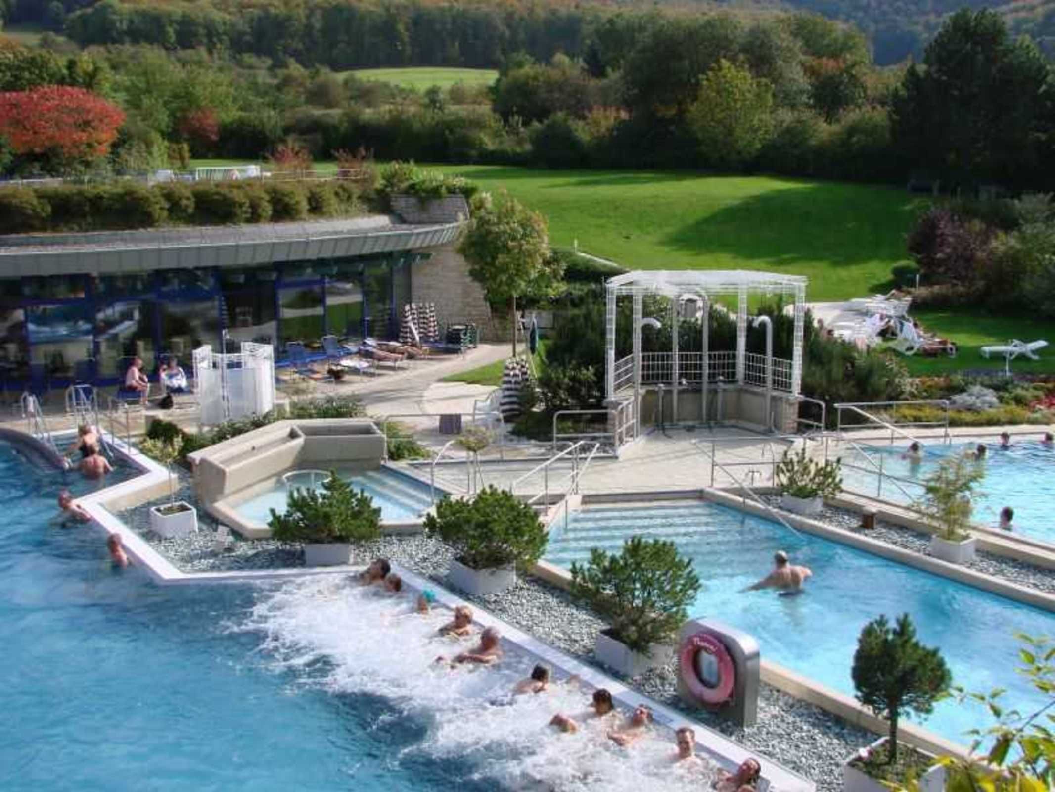 Area piscina con diverse piscine, uno scivolo acquatico e una zona relax coperta.