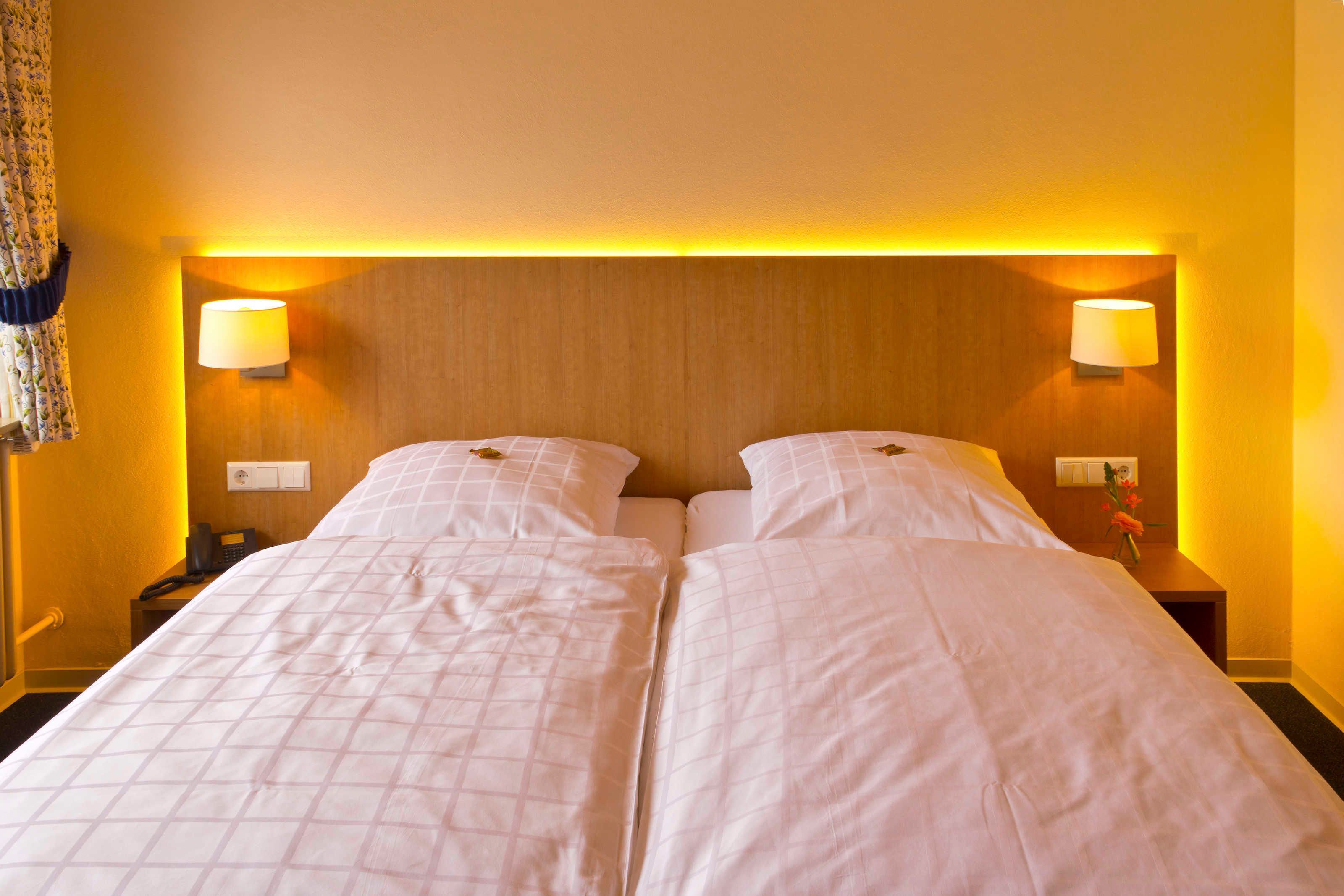 Un letto matrimoniale con poggiatesta in legno, due lampade sui comodini e un telefono.