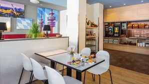 Una cafetería moderna con mostrador, zona de estar y exhibición de pasteles y bebidas.