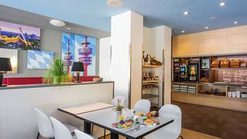 A modern cafe with a counter, seating area, and a display of pastries and beverages.
