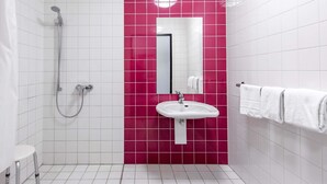 Un baño con azulejos blancos, una pared de acento rosa, un lavamanos, un espejo y una ducha.