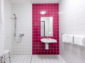 A bathroom with white tiles, a pink accent wall, a sink, a mirror, and a shower. - B&B Hotel München City-Nord (Munich)