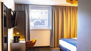 Una habitación de hotel con cama, escritorio con lámpara, silla y televisor.