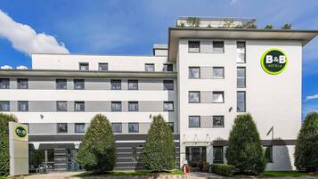 A B&B hotel with a modern design, featuring a flat roof, large windows, and a well-maintained garden with neatly trimmed bushes.