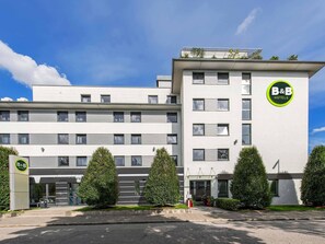A B&B hotel with a modern design, featuring a flat roof, large windows, and a well-maintained garden with neatly trimmed bushes. - B&B Hotel München City-Nord (Munich)